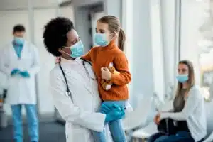 A female doctor smiling and holding a young girl who is also smiling and happy after Cold & Flu Treatment