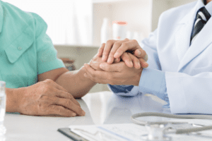 A primary care physician gently holding a hand of a senior male patient