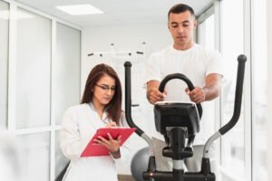 A male athlete training on a stationary elliptical machine while a female medical professional in a lab coat tracks his progress on a clipboard
