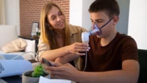 A woman assisting a young boy as he uses a nebulizer mask for respiratory treatment at home