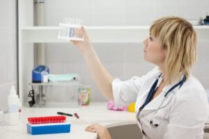 A female medical professional in a lab coat examining a test tube from a rack in a clinical laboratory setting